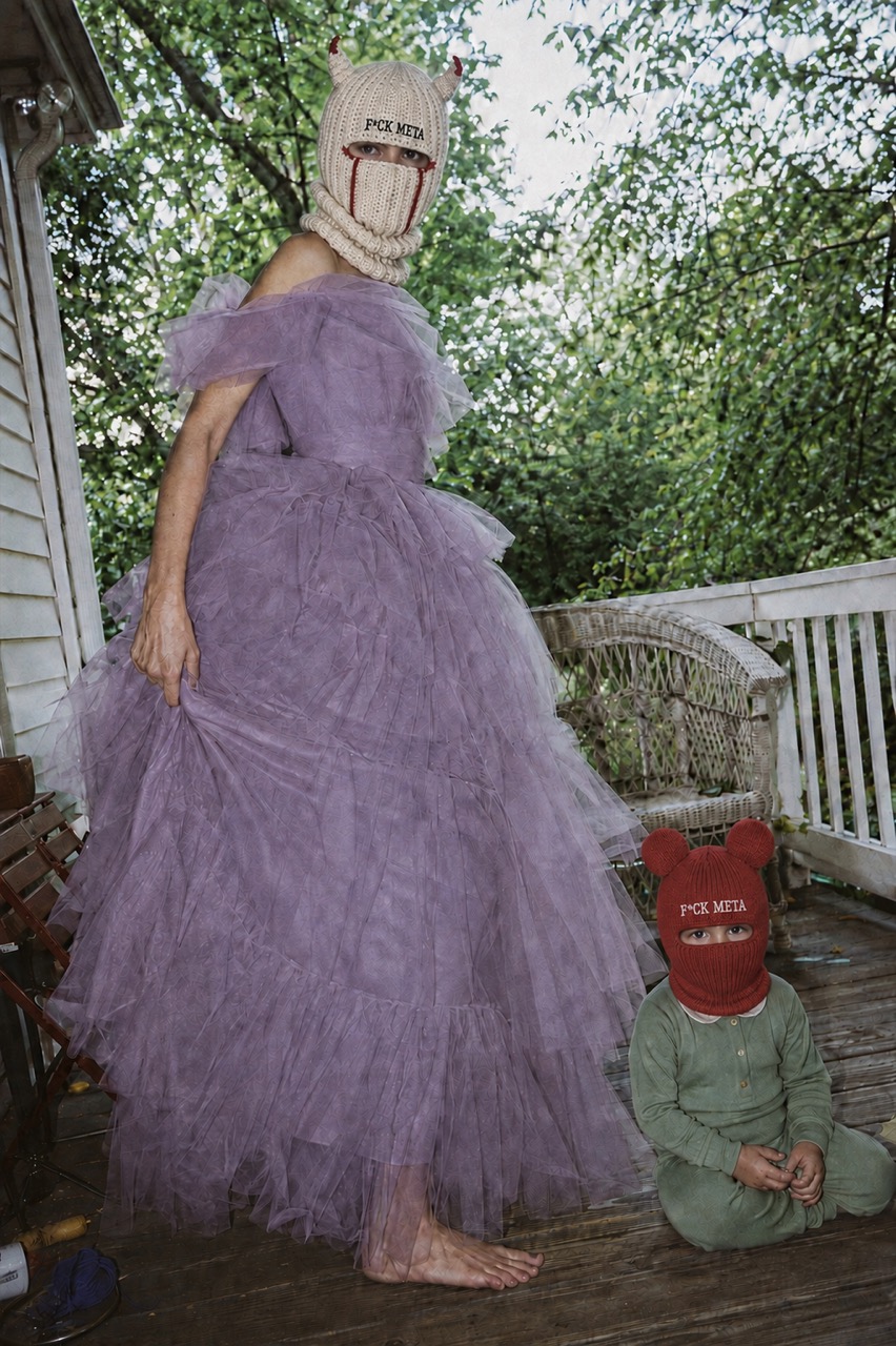 A woman in a purple tulle gown and horned ivory F*CK META balaclava on a porch, a child beside her in a red F*CK META balaclava.